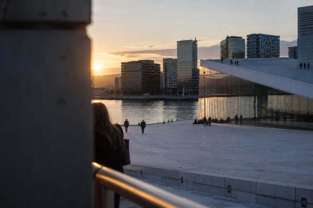 Modern waterfront skyline of glass towers and an opera house roof at dusk