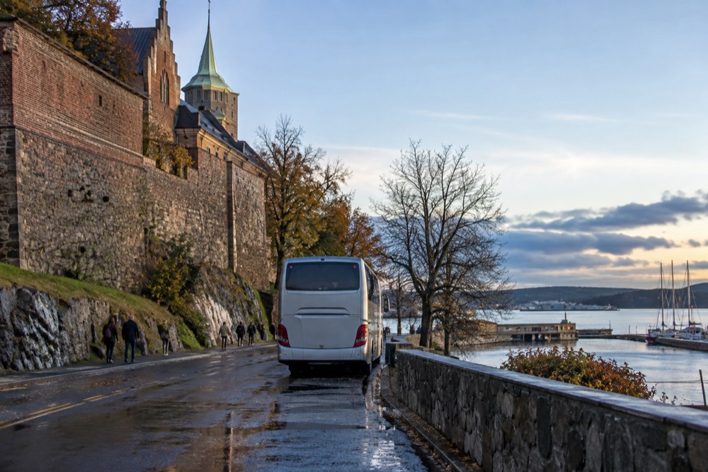 Sightseeing bus parked near the Akershus fortress walls with the harbor beyond
