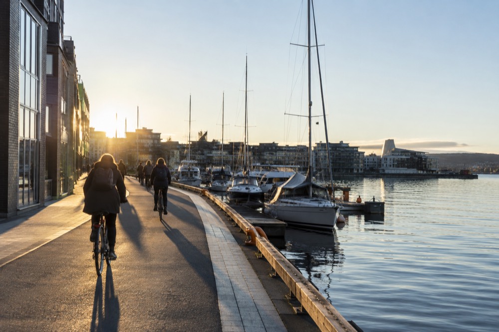 Cyclists on a waterfront path beside the Oslofjord with moored boats in the background