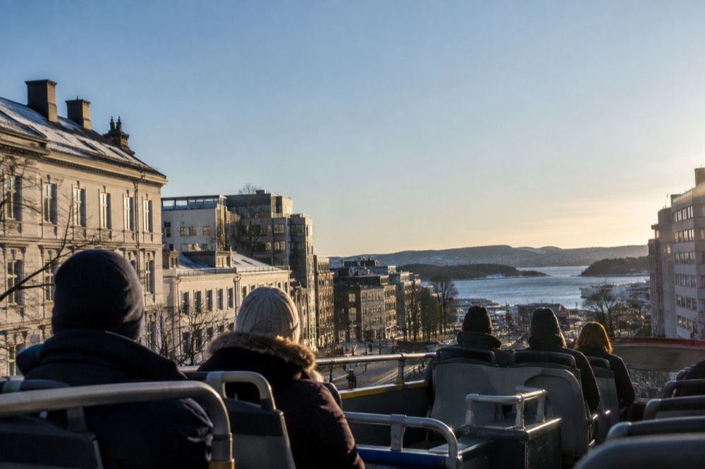 Top deck of a sightseeing bus with views over Oslo rooftops toward the fjord