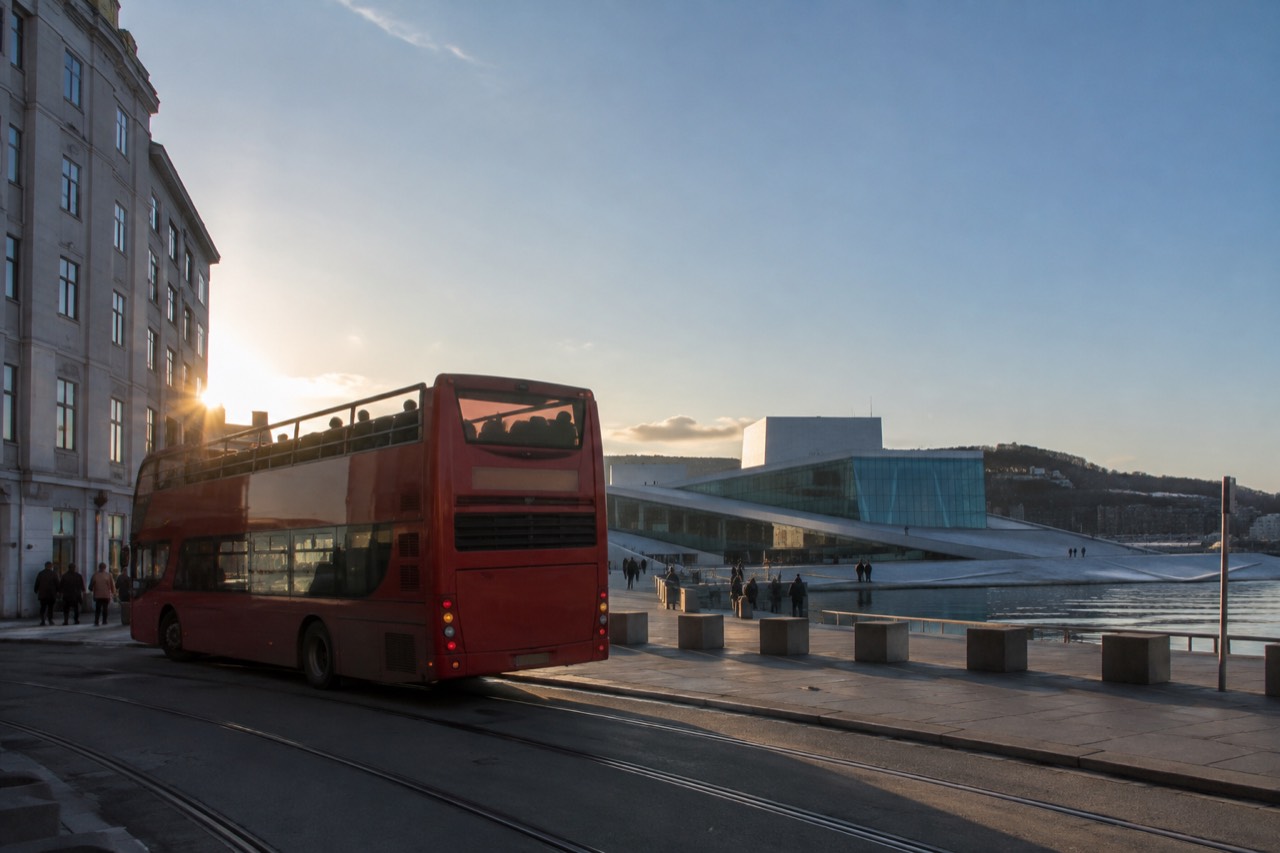 Red open-top sightseeing bus parked on an Oslo street with the Opera House in the background