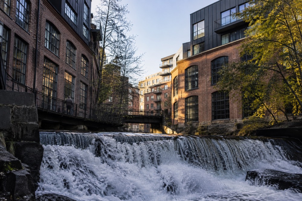 The Akerselva river flowing past converted brick mill buildings with a waterfall in the foreground