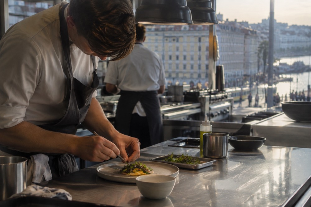 Chef plating a small course with tweezers in a restaurant kitchen