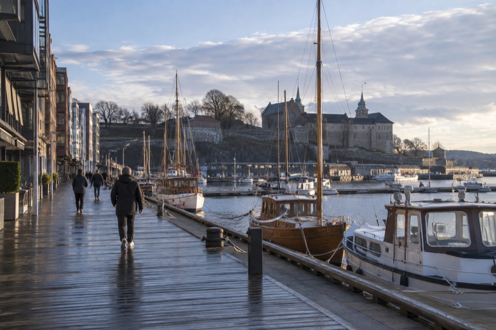 Aker Brygge boardwalk with wooden piers and moored boats facing Akershus Fortress