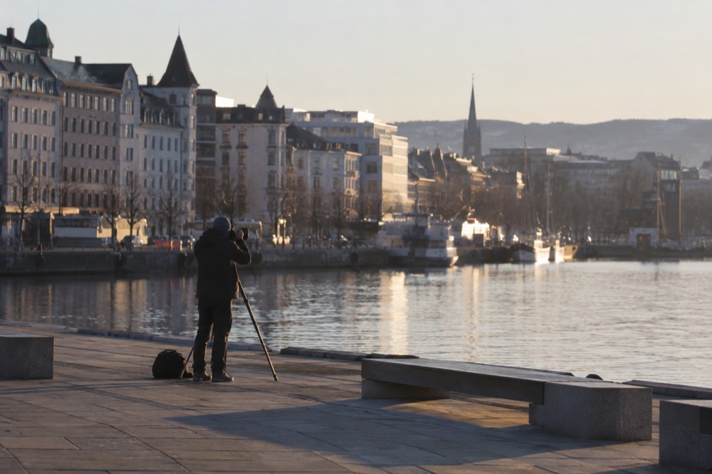 Photographer with a tripod on an empty waterfront promenade at dawn