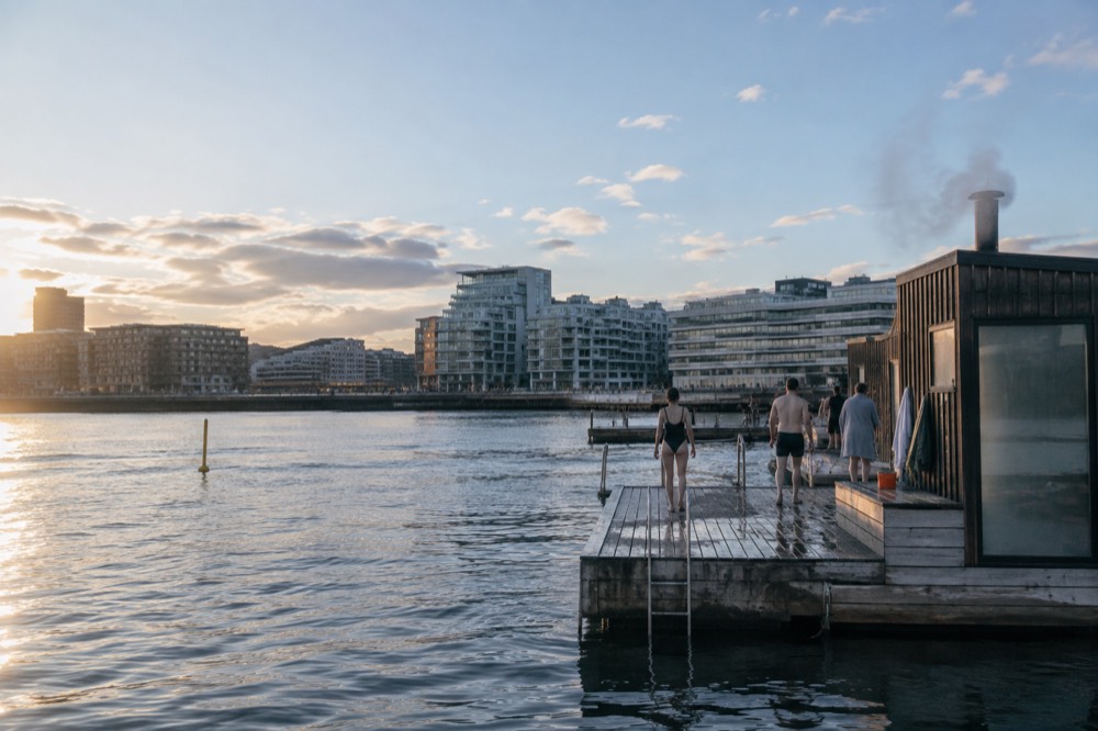 Bathers walking on a floating sauna pier at Sørenga with steam rising from the cabin