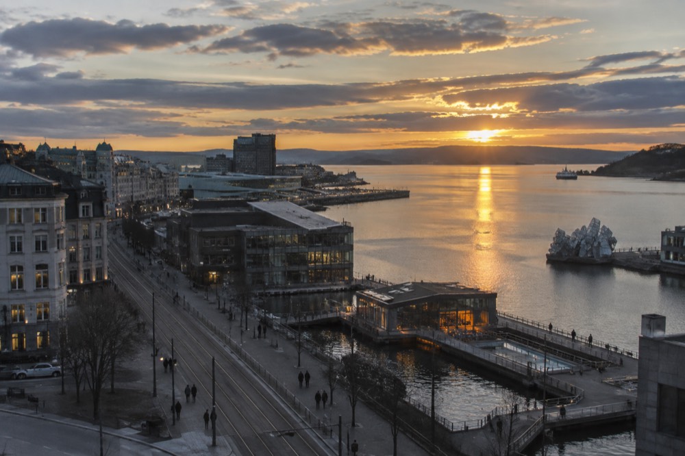 Evening view across the Oslofjord with lit sauna windows and the city reflected in calm water