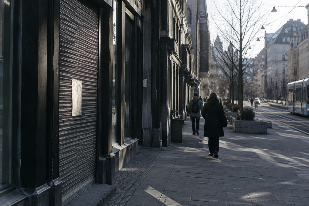 Closed shopfront with a handwritten hours sign on a quiet street