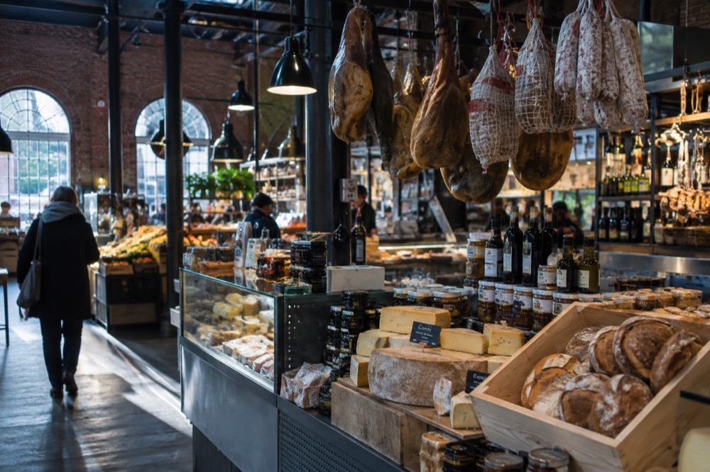 Food hall stalls with cheeses, breads, and cured meats under indoor lights