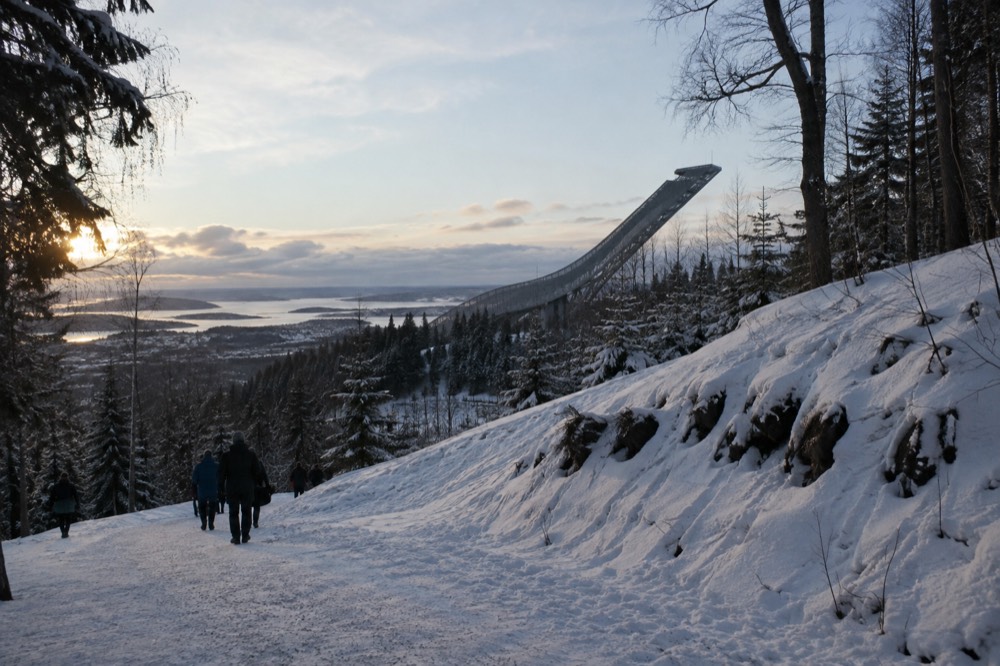 Steel ski jump tower rising above snowy forest with a viewing platform at the top