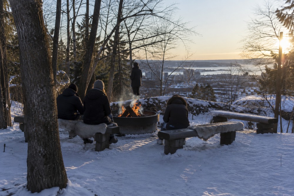 Campfire burning in a snowy forest clearing with benches arranged around it
