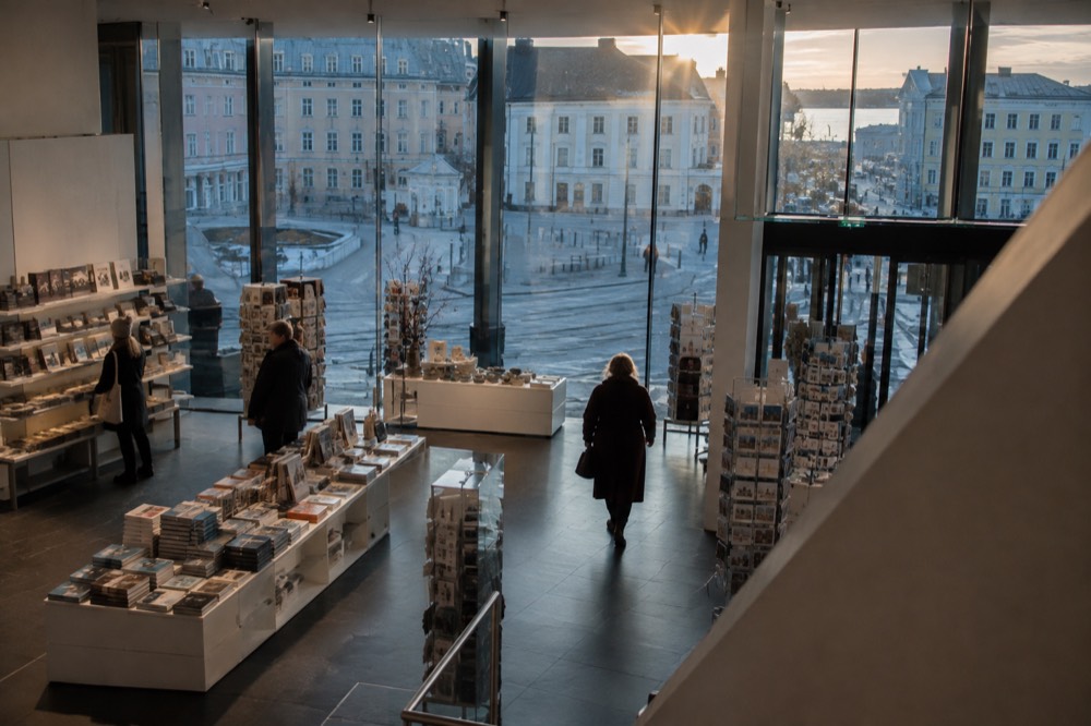 Museum shop interior with books, postcards, and design objects displayed on wooden tables