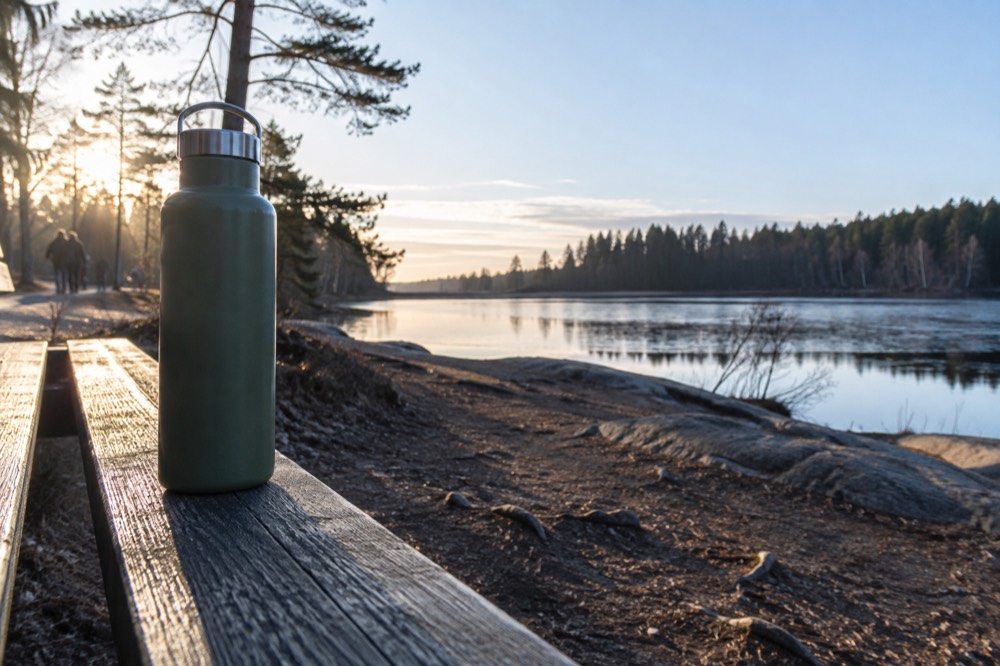 A refillable water bottle resting on a wooden bench beside a forest lake in Oslo