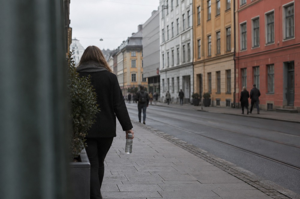 A person holding a water bottle while walking past colorful Oslo buildings