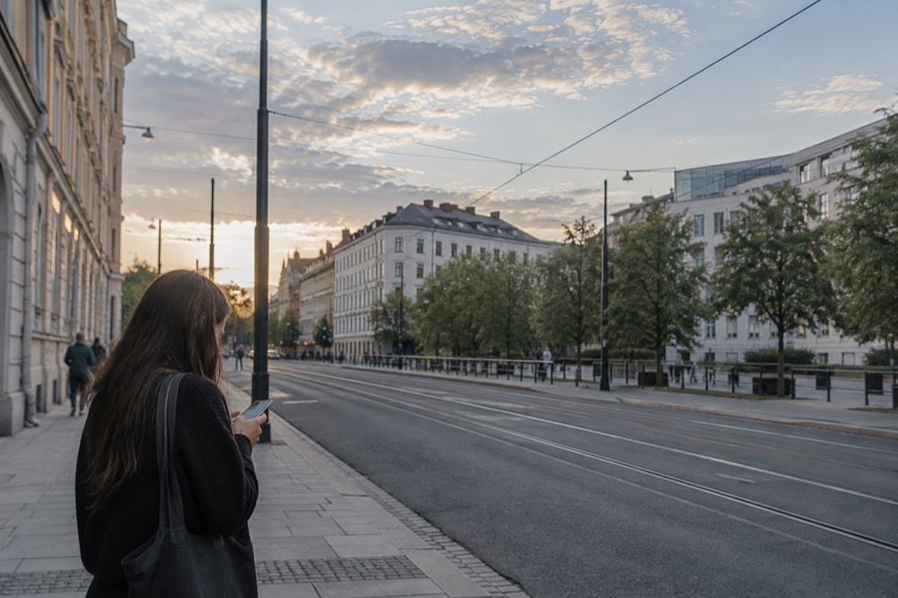 Person checking a rideshare app on a phone beside a quiet Oslo street at dusk