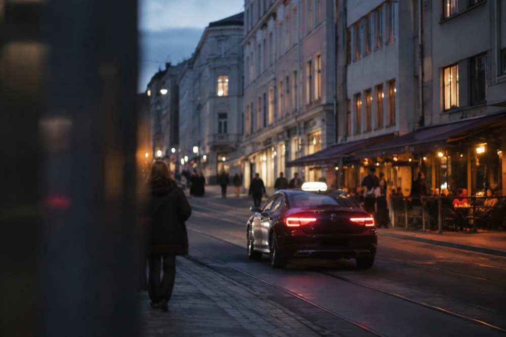 Well-lit Oslo street at night with a taxi passing a bar district