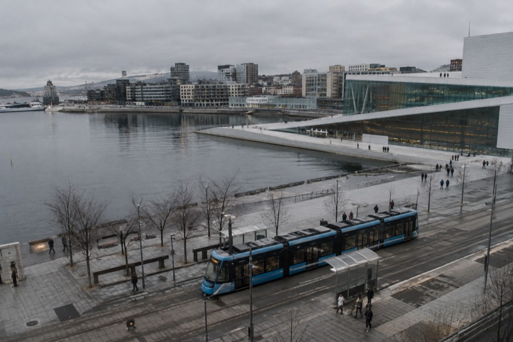 A tram traveling past the Oslo Opera House and modern waterfront buildings