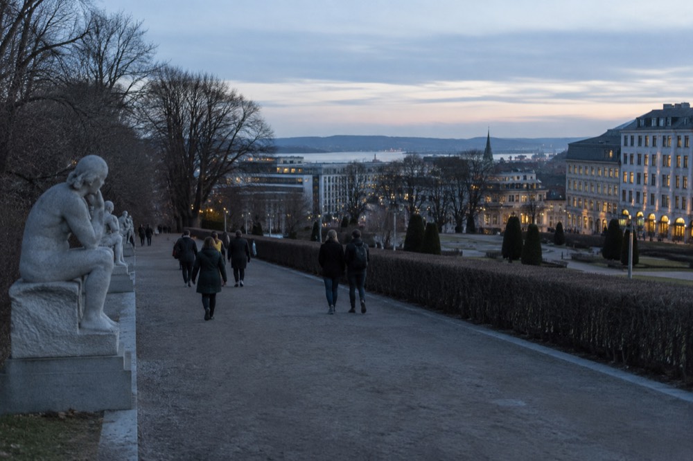 People walking a wide park path lined with large stone sculptures