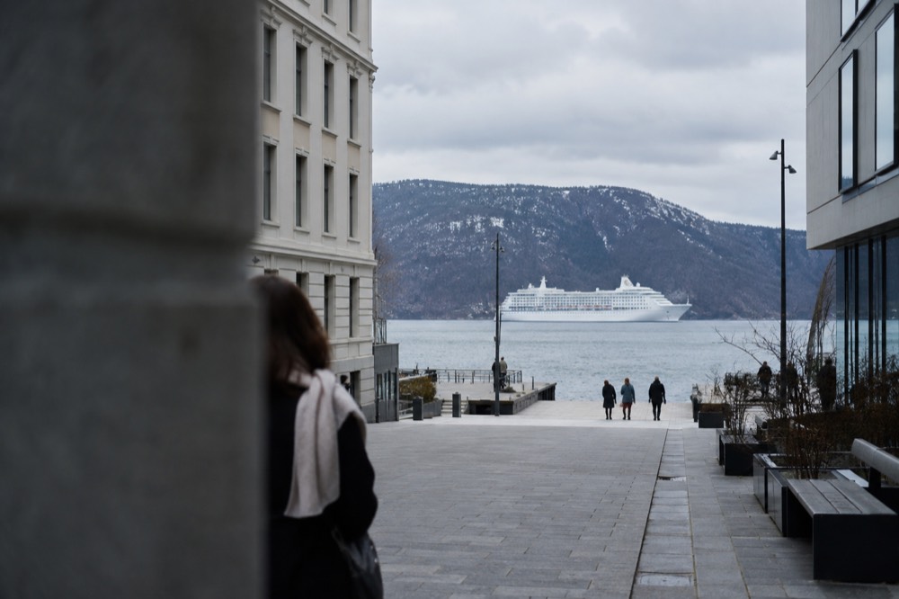White cruise boat on calm green fjord water beneath steep cliffs