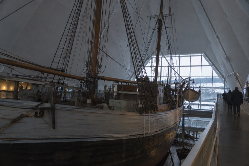 Wooden polar expedition ship displayed inside a museum hall with visitors on walkways