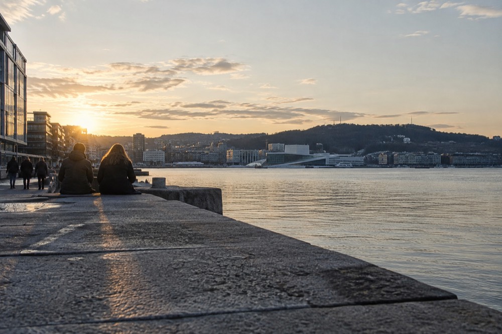 City skyline at dusk seen across open water with forested hills behind