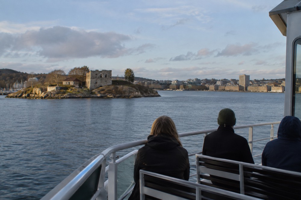 A small island with rocky shores and a stone ruin seen from a passenger ferry