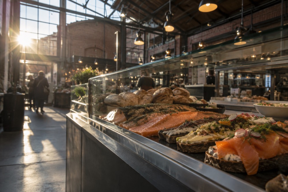 A food hall counter with cured fish, breads and open sandwiches arranged behind glass