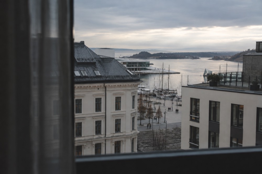 A hotel room window overlooking rooftops and a harbor with morning light