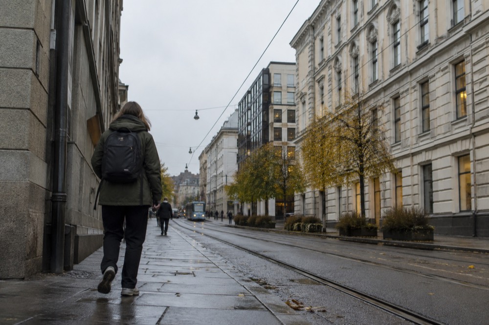 A person in a rain jacket and backpack walking an Oslo street in autumn