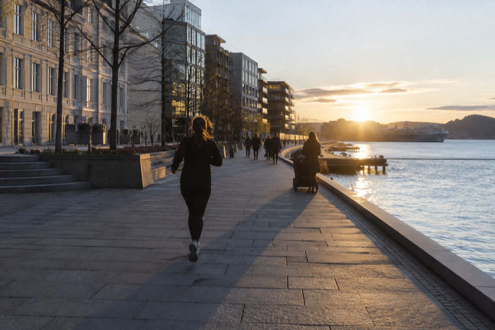 A wide flat waterfront promenade with a stroller and calm fjord water beyond