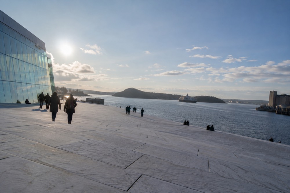 A sloping marble opera house roof with a harbor and fjord beyond