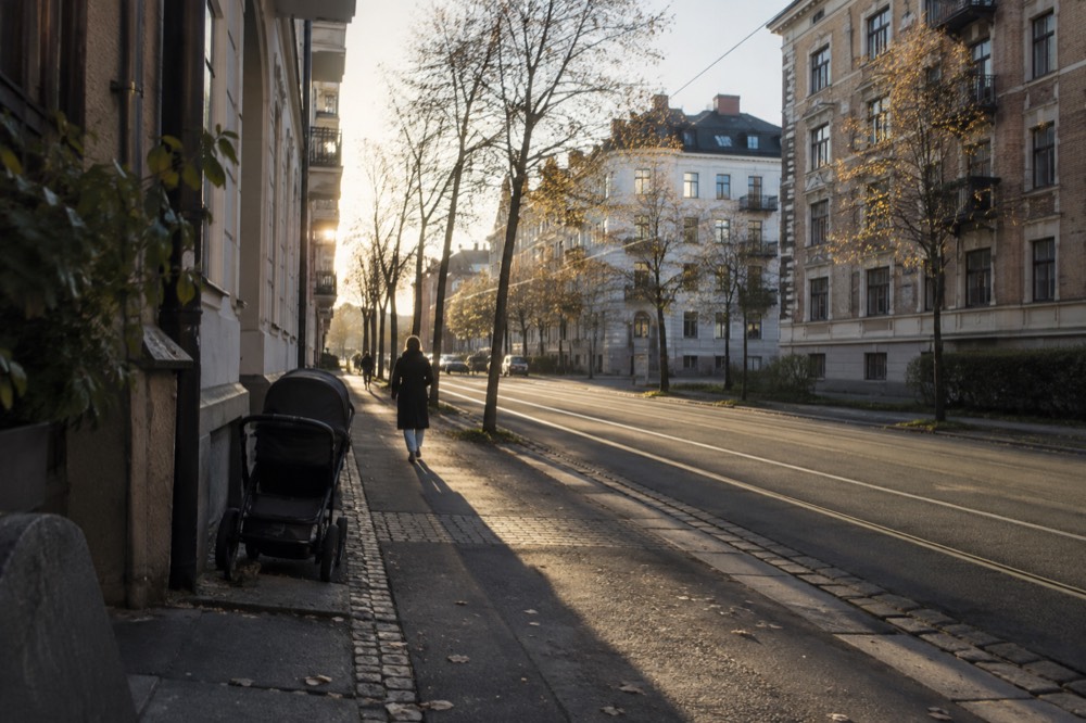 A calm residential street of brick apartment buildings with trees and a parked stroller
