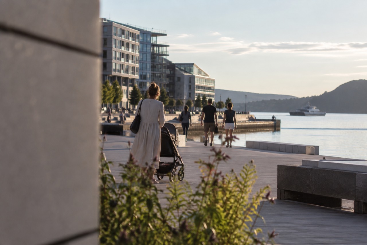 A stroller on a wide Oslo waterfront promenade beside calm fjord water