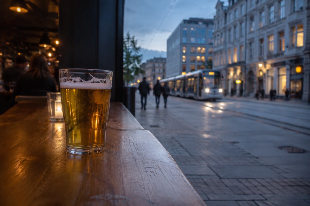 A pint glass of pale beer on a bar counter with blurred pub lights behind