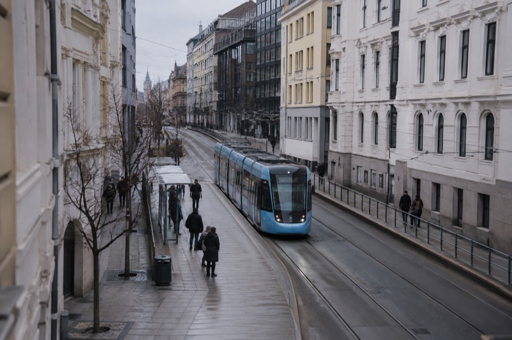 A tram moving along a street in central Oslo with passengers waiting at a stop
