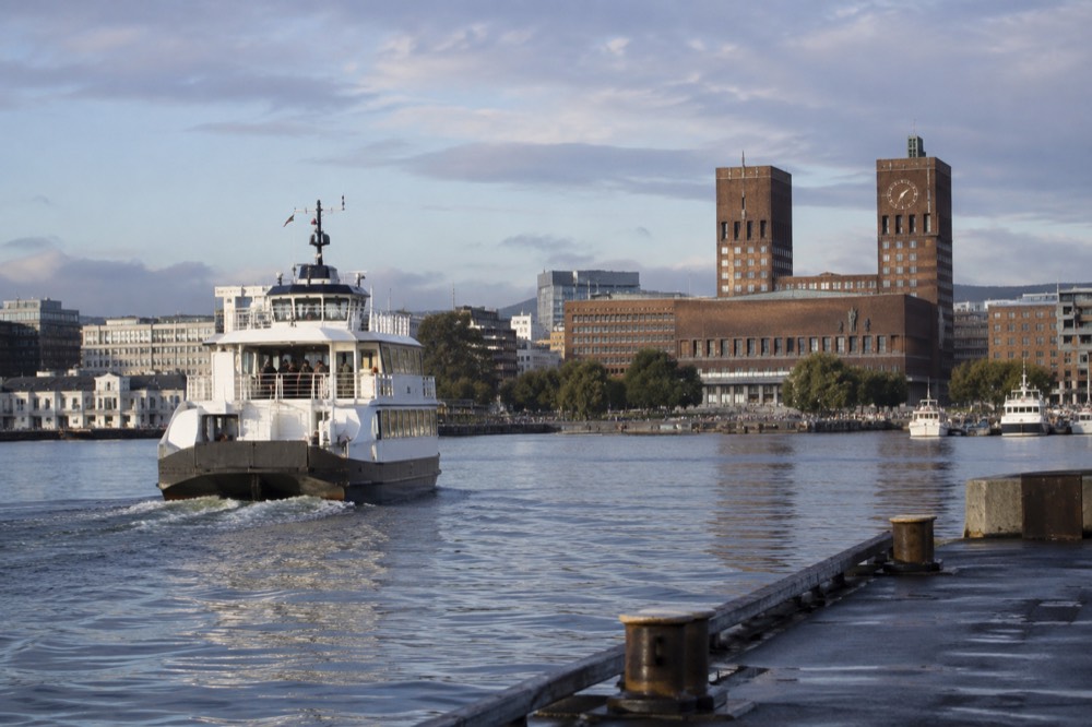 A ferry departing a pier in Oslo harbor with the city hall behind it