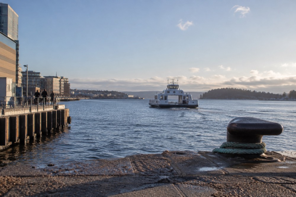 A small passenger ferry on the water between Oslo and a forested island