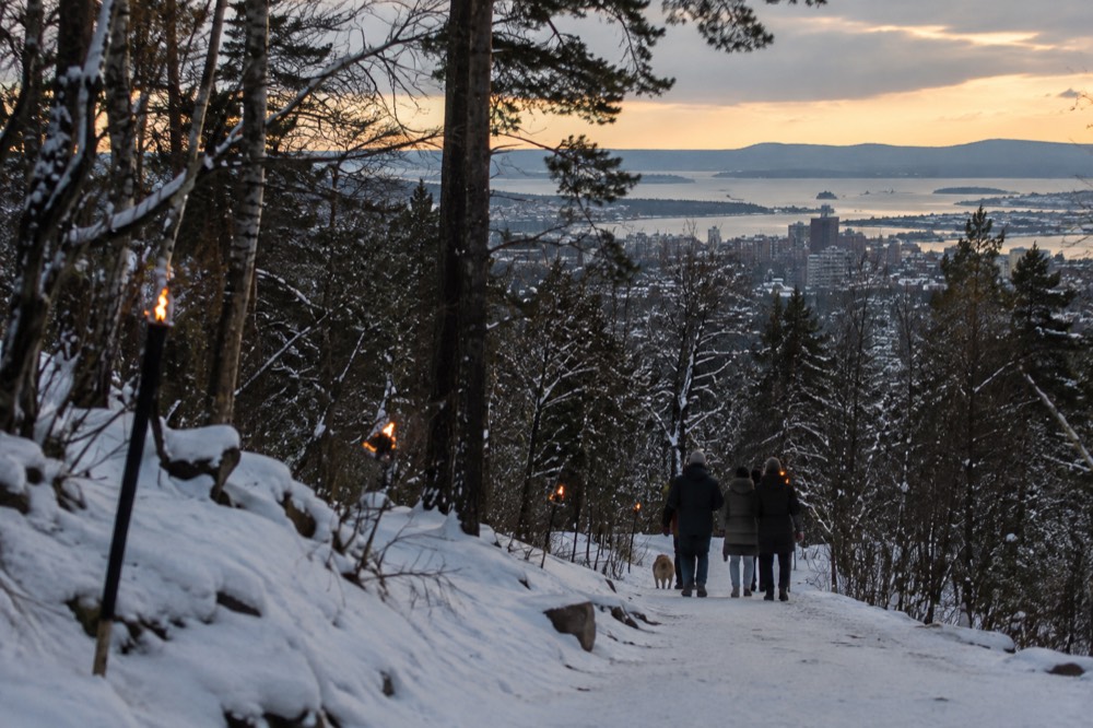 Snow-covered forest trail with torchlights above Oslo at dusk
