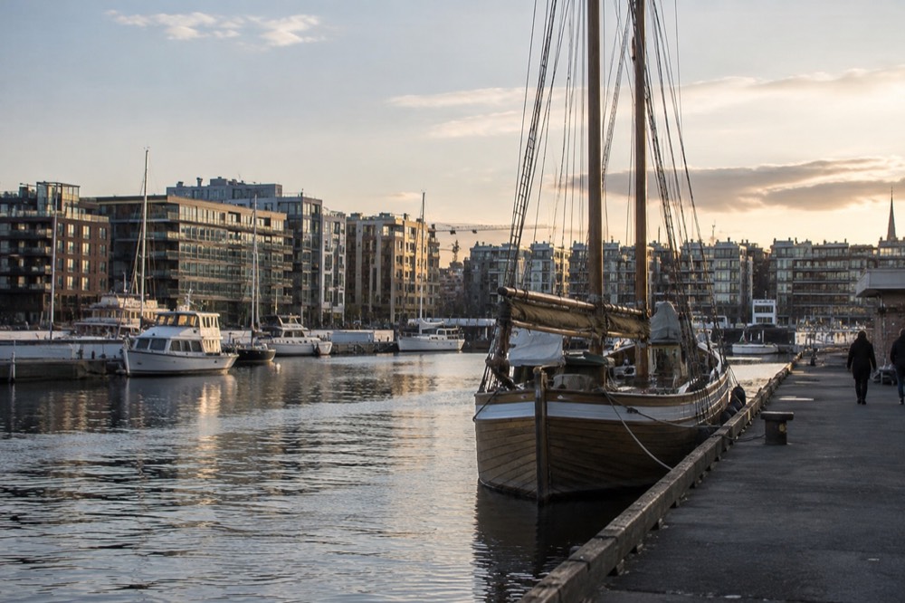 Wooden sailing ship moored in Oslo harbor with apartment buildings behind