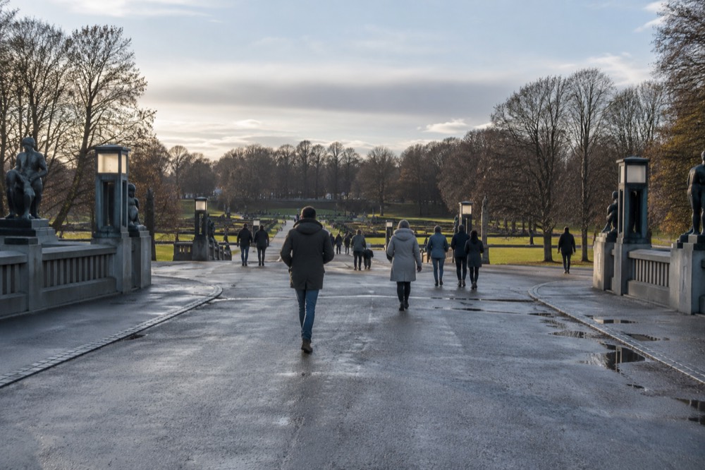 People strolling across open lawns and wide granite paths in Frogner Park on a mild day