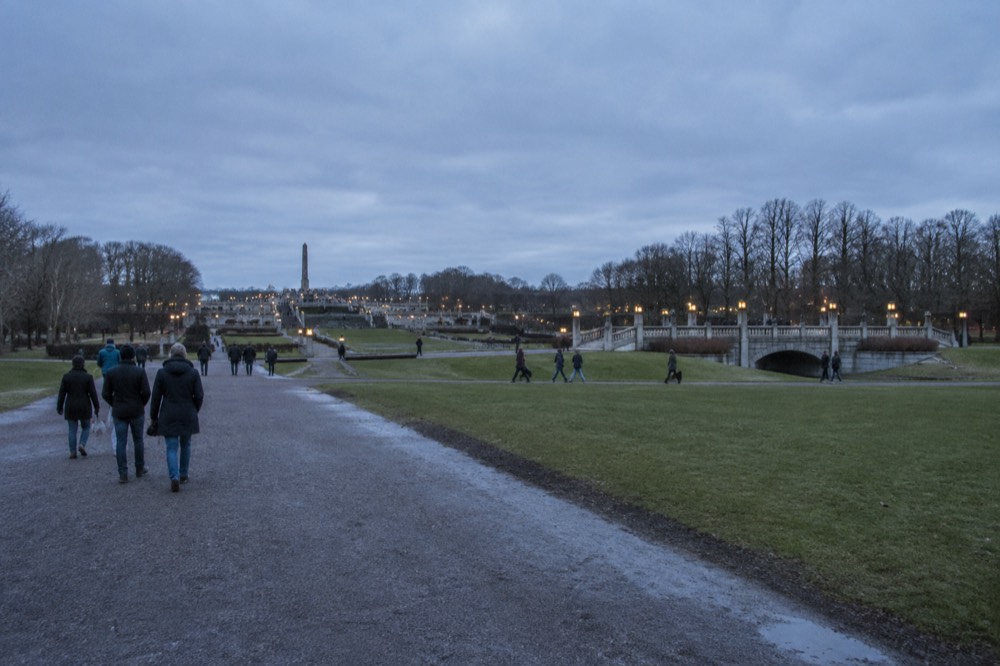 Visitors walking the broad lawns and granite walks of Vigeland Park under a gray sky