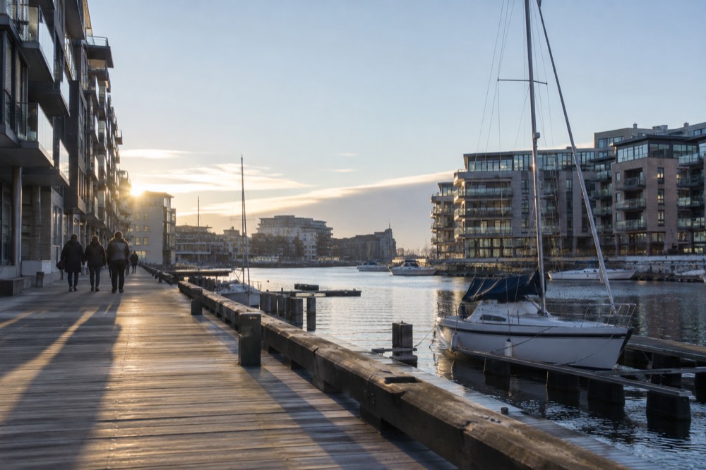 Wooden boardwalk along a city harbor with moored boats and apartment buildings