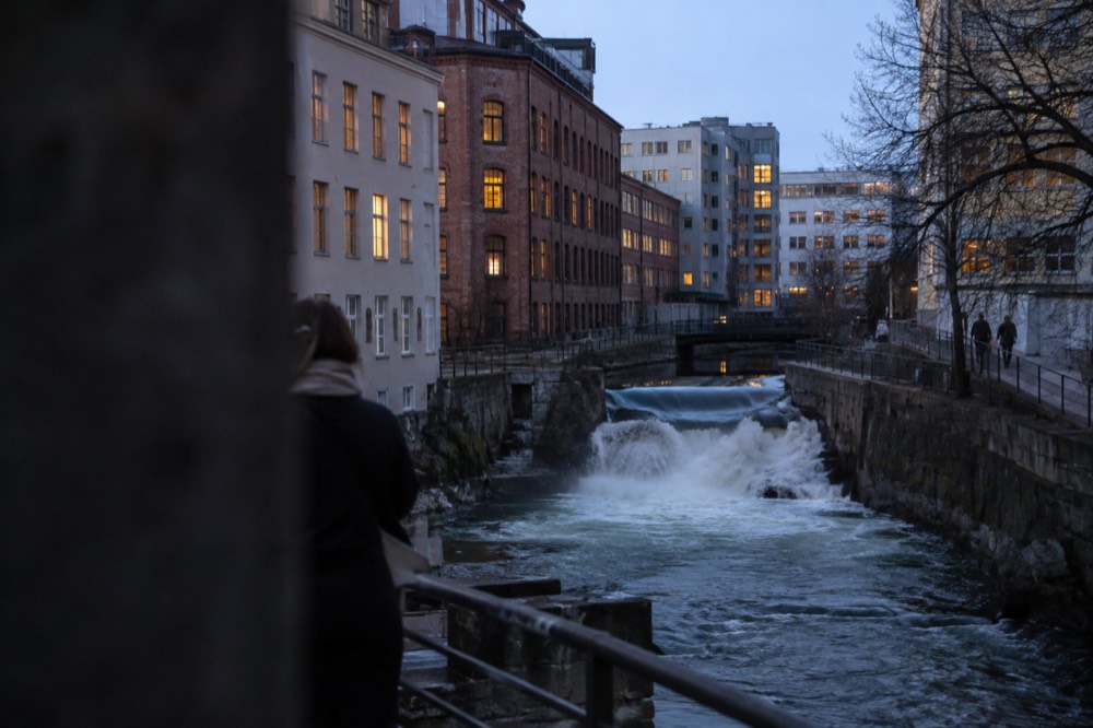 A green river running between old factory buildings with a small waterfall