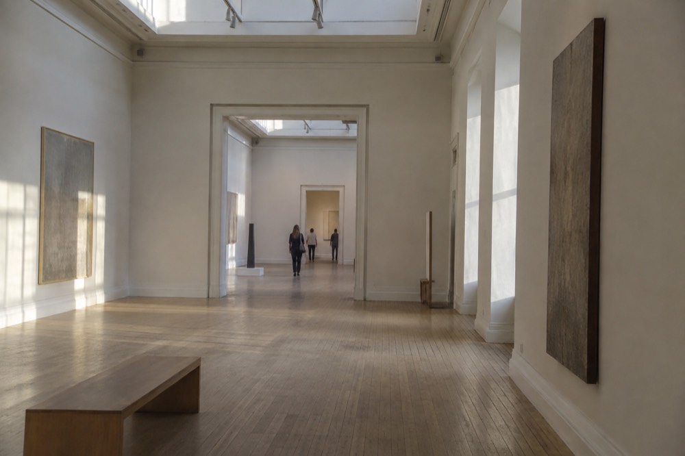 A quiet museum interior in Oslo lit by skylights, with pale plaster walls and wooden floors