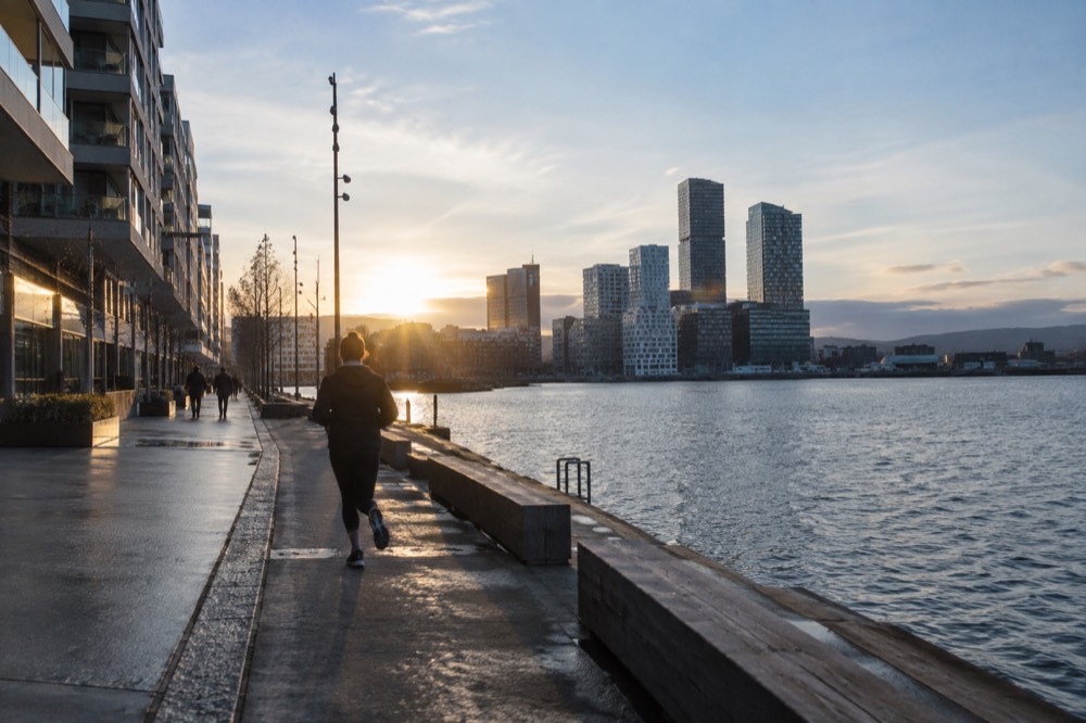 Narrow modern glass towers seen from a waterfront promenade at dusk