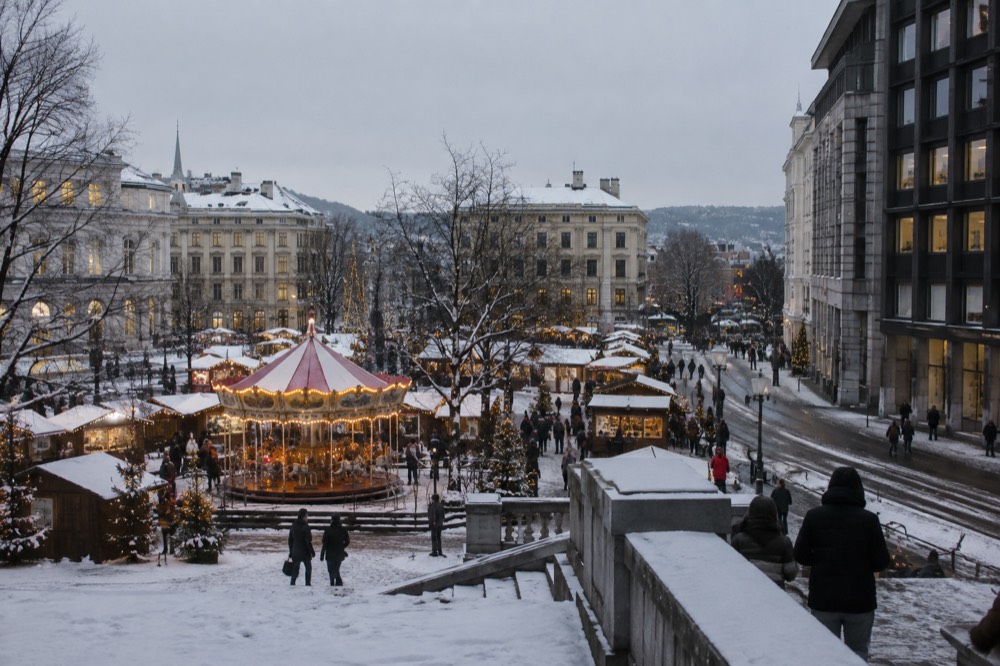 Christmas market stalls with lights and a carousel on a snowy Oslo square