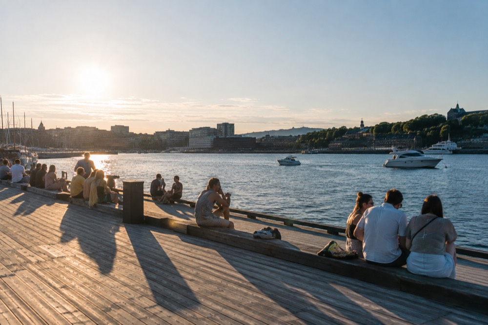 People sitting outside on a sunny pier in Oslo with boats on the water