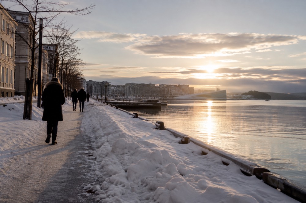 Snow-dusted waterfront promenade in Oslo with low winter light on the fjord