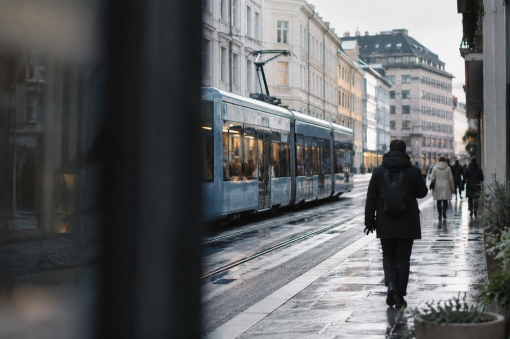 Tram moving along an Oslo street with pedestrians on the sidewalk