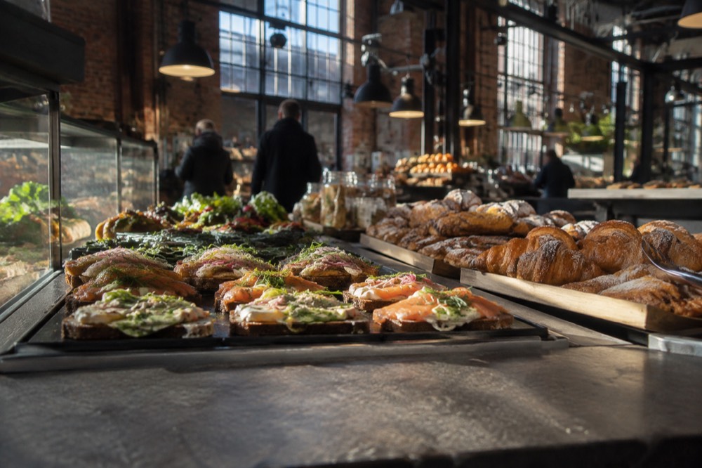 A food hall counter with trays of open sandwiches and pastries
